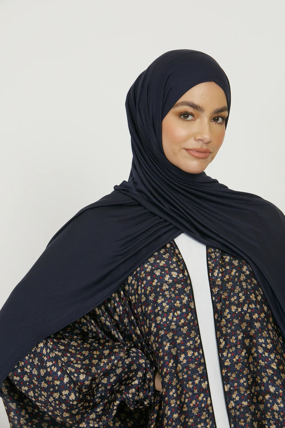 Eine Frau trägt einen dunkelblauen Jersey-Hijab und ein gemustertes Oberteil.