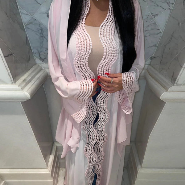 A woman wearing an elegant pink maxi kaftan dress with white embroidery in a marble staircase setting.