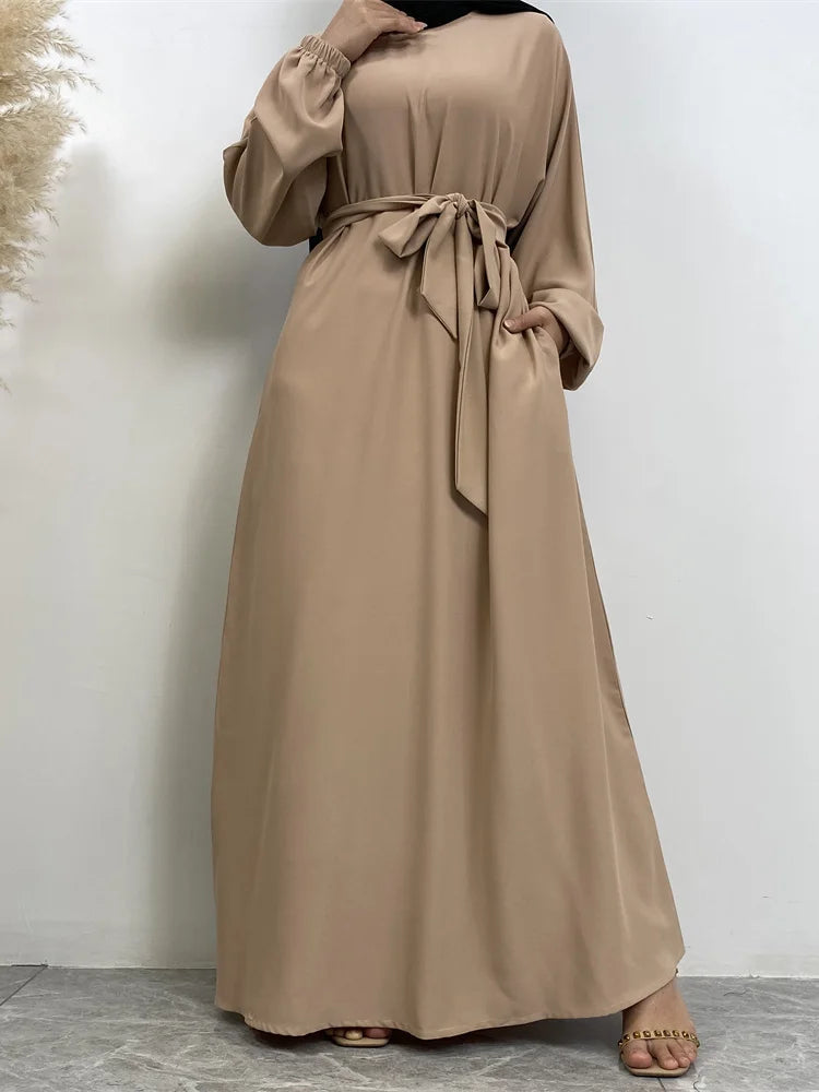 Eine Frau trägt ein beige marokkanisches Kaftan-Abaya mit langen Ärmeln und einem zugebundenen Bund.