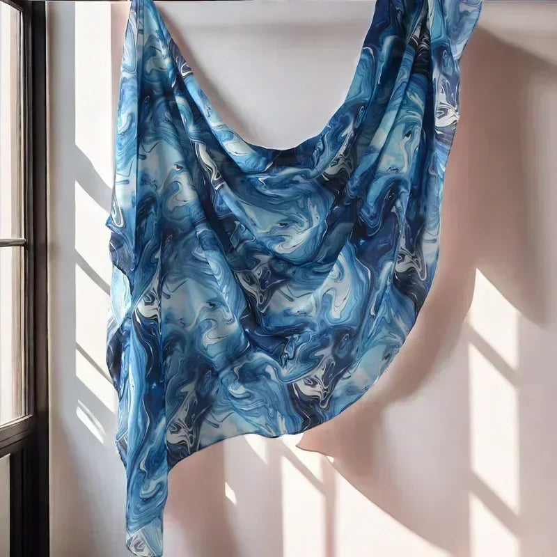 Blau-weißes, floral gedrucktes Aquarell-Schal über einer hellen Wand drapiert.