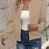 Une femme portant une veste à fermeture éclair tricotée beige sur un haut blanc et un jean bleu.