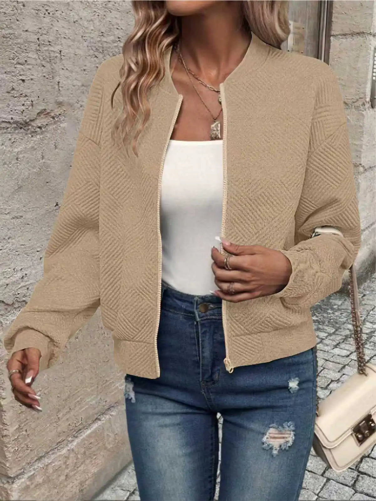 Une femme portant une veste à fermeture éclair tricotée beige sur un haut blanc et un jean bleu.