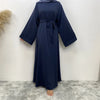 Abaya elegante de encaje azul marino para mujer colgada contra una pared blanca.