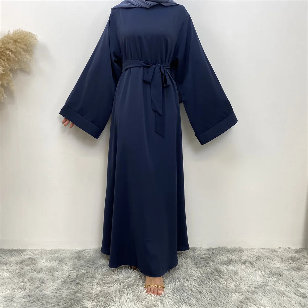 Abaya elegante de encaje azul marino para mujer colgada contra una pared blanca.