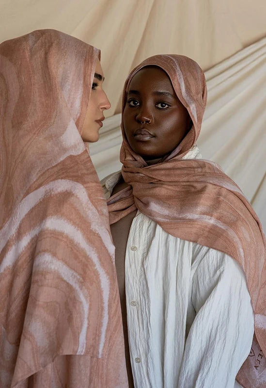 Retrato de cerca de una mujer vistiendo un pañuelo hijab estampado leopardo color rosa polvoriento y ropa blanca.