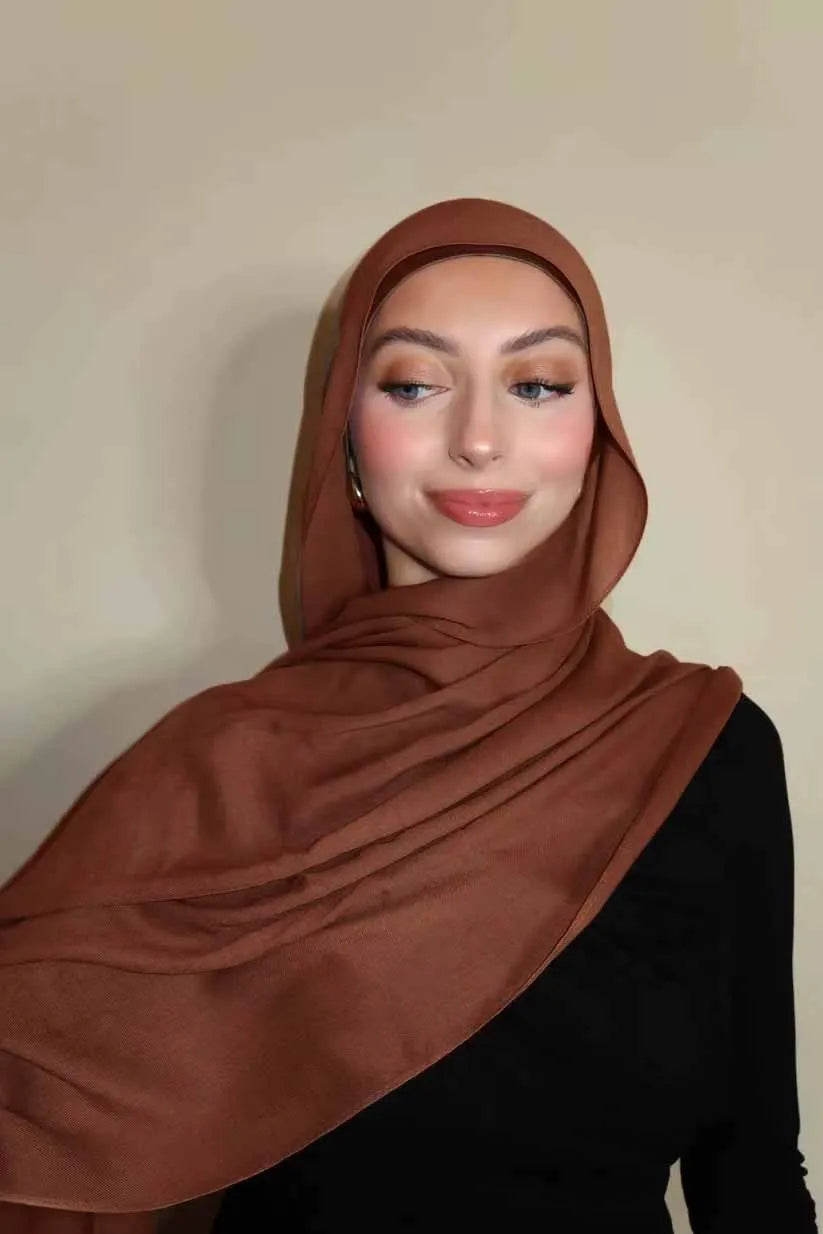 Eine Frau trägt einen einfarbigen braunen Gradient-Rayon-Modal-Hijab und schwarze Kleidung.