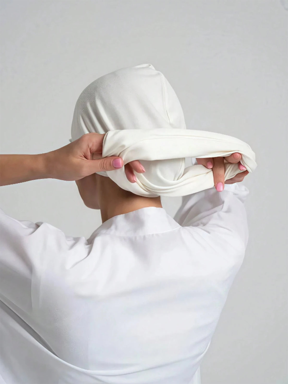 Une personne ajuste un foulard instant hijab blanc sur sa tête.
