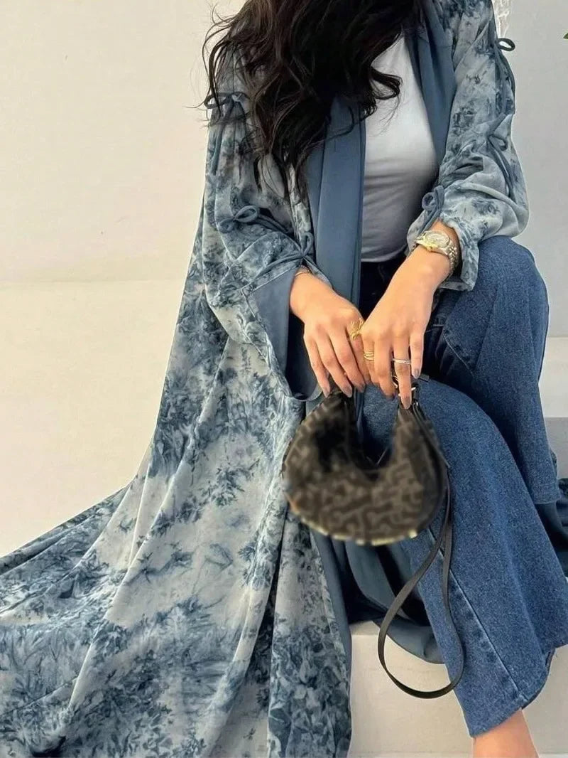 Eine Frau trägt einen blau-blumigen Tie-Dye-Kaftan über einem weißen Top und blauen Jeans.