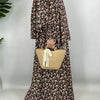 Una mujer vistiendo una elegante kaftan abaya floral con mangas largas y tela estampada, sosteniendo una bolsa de paja tejida