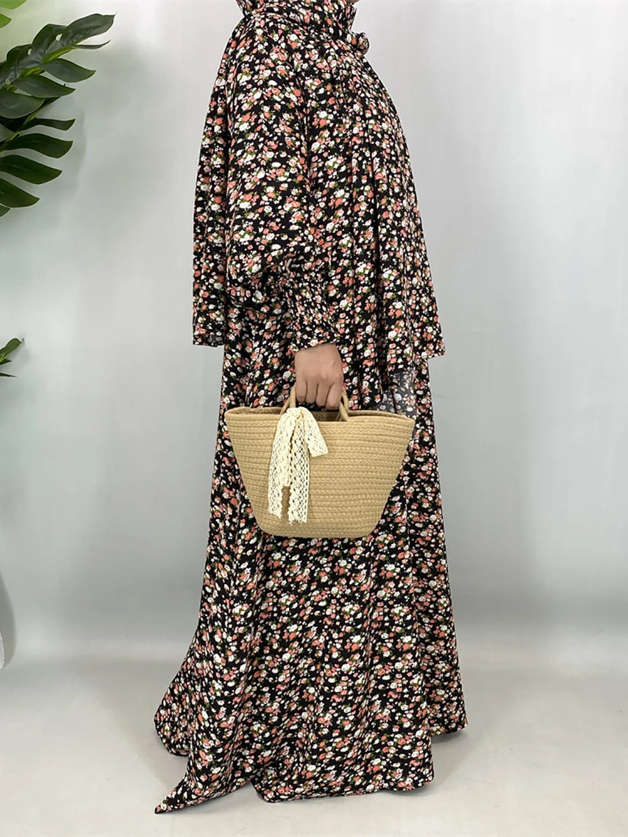 Una mujer vistiendo una elegante kaftan abaya floral con mangas largas y tela estampada, sosteniendo una bolsa de paja tejida