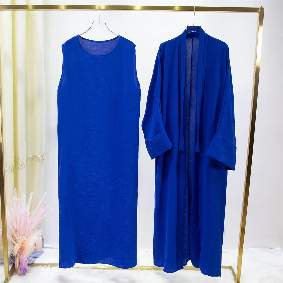 Jilbab de dos piezas azul real para mujer, exhibido en percha dorada contra fondo blanco.