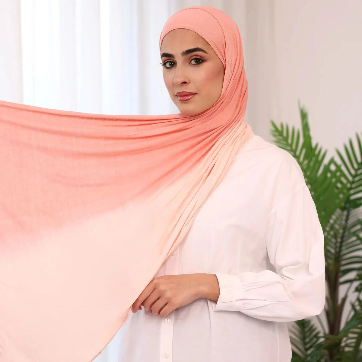 Una mujer vistiendo un pañuelo de hijab de algodón con degradado melocotón de doble cara y una blusa blanca.