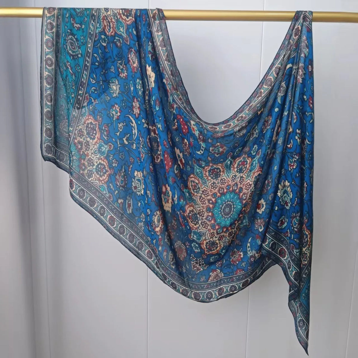 Lebendiges blaues und türkisfarbenes Mehrfarbiges Hijab-Schal hängt an einem Holzstab.