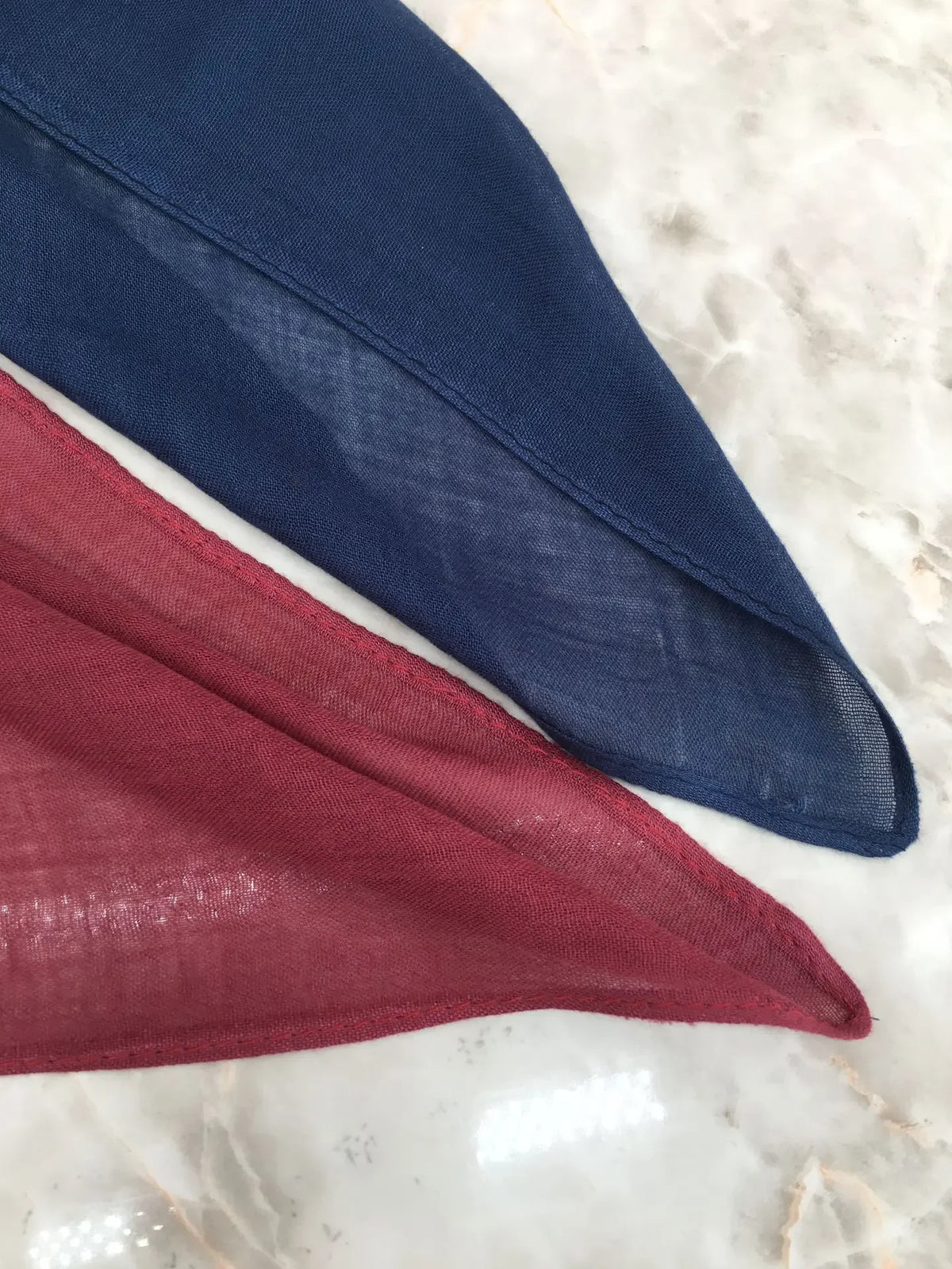 A close-up of a navy blue and maroon soft modal rayon hijab set fabric laid on a white marble surface.