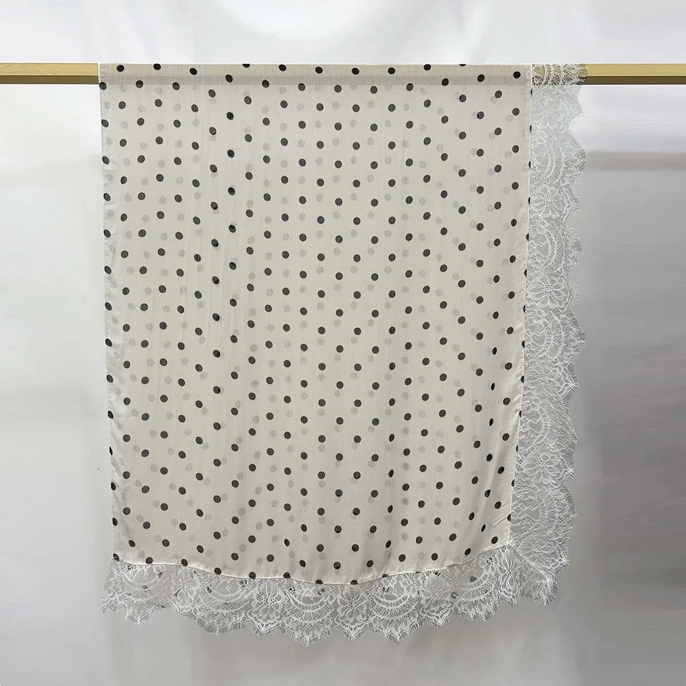 Tela de hijab color crema con estampado de lunares grises y un ribete de encaje ornamentado.