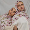 Une femme portant un hijab floral aquarelle rose et un haut blanc, regardant directement l'appareil photo.