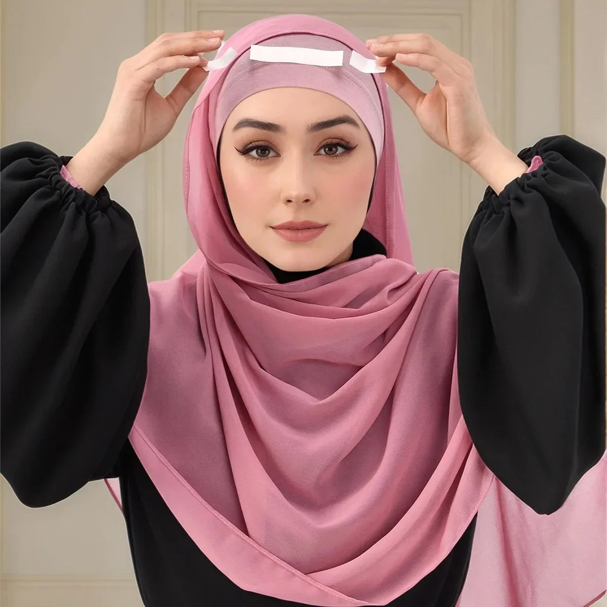 Una mujer con un hiyab rosa está usando cinta corporal invisible para asegurar su pañuelo.