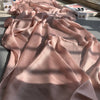 Fließender rosa Crinkle-Satin-Chiffon-Hijab, drapiert auf einer Oberfläche mit Schatten.