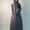 Una mujer vistiendo un cárdigan abaya plisado largo a rayas grises y un pañuelo negro para la cabeza.