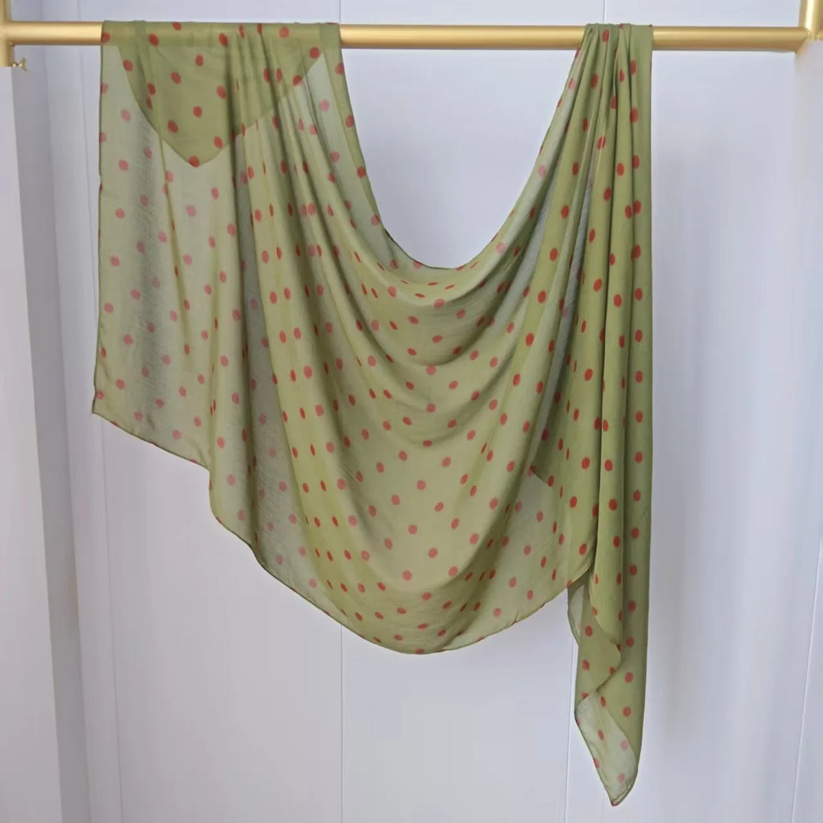 Pañuelo modal verde claro transparente con pequeños puntos rosas colgado en un perchero de madera.