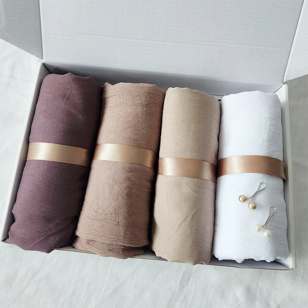A box containing a 4-piece crinkled cotton Muslim hijab scarf set with purple, beige, and white scarves.