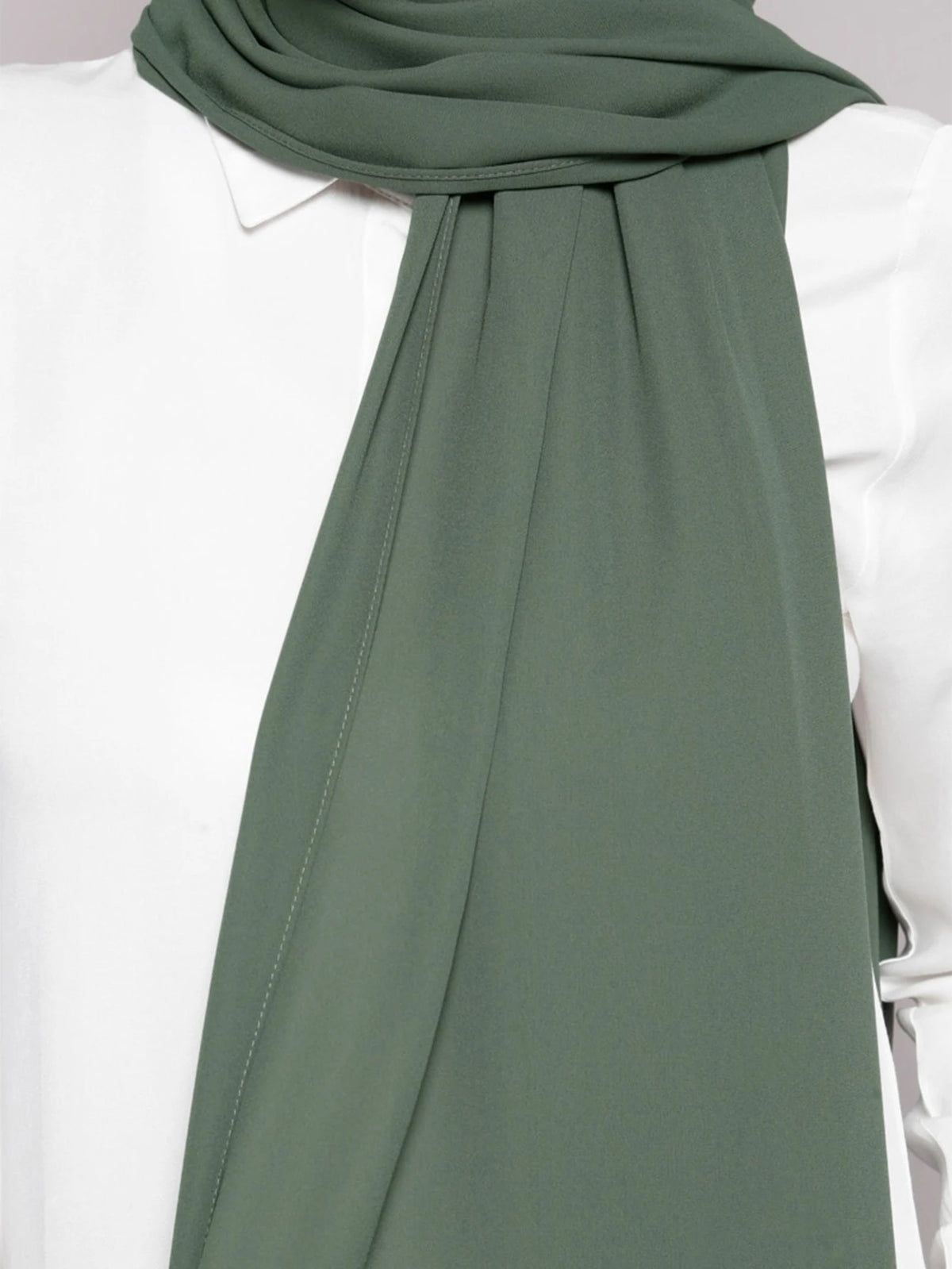 A close-up of a sage green chiffon scarf draped around the neck, paired with a white top.