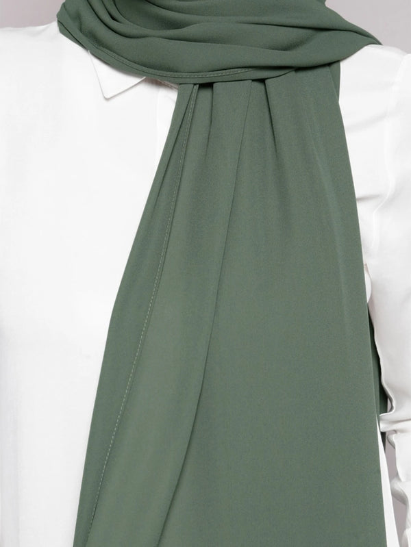 A close-up of a sage green chiffon scarf draped around the neck, paired with a white top.