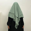 A woman wearing a light sage green two-layer everyday hijab scarf over a black top.