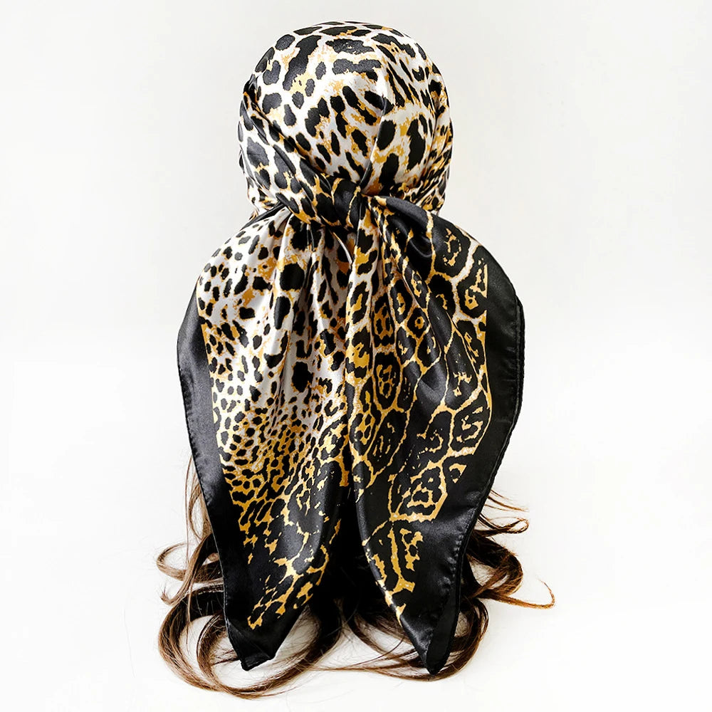 Pañuelo de seda cuadrado estampado leopardo negro y dorado atado en un nudo, con cabello espeso visible abajo.