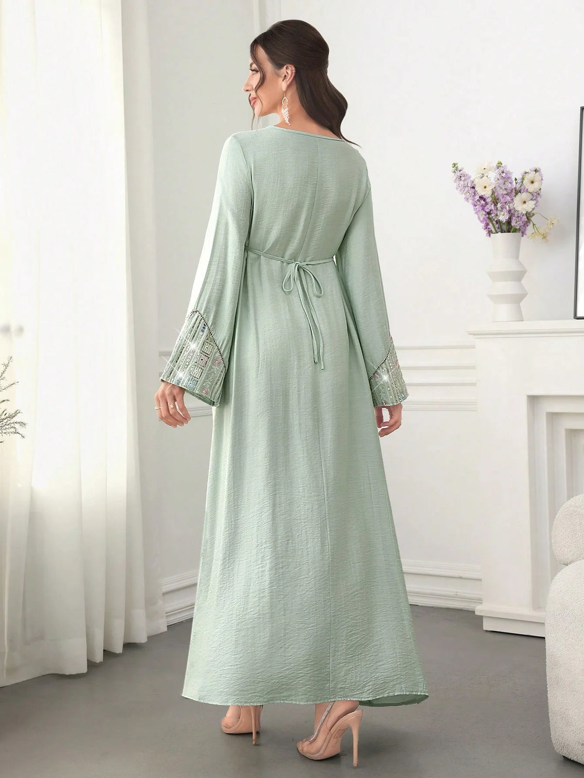 Eine Frau präsentiert eine hellgrüne Abaya mit Paillettenstickerei und einem Gürtel in einer Ganzkörperaufnahme.
