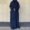 A dark blue elegant two-piece abaya and khimar set worn by a person against a light stone wall.