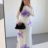 Eine Frau modelliert ein elegantes weißes Abaya-Kleid mit lila Blumenmuster, langen Ärmeln und hohem Ausschnitt.
