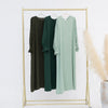 Un vestido abaya holgado de color verde oliva cuelga en una percha dorada contra un fondo blanco.