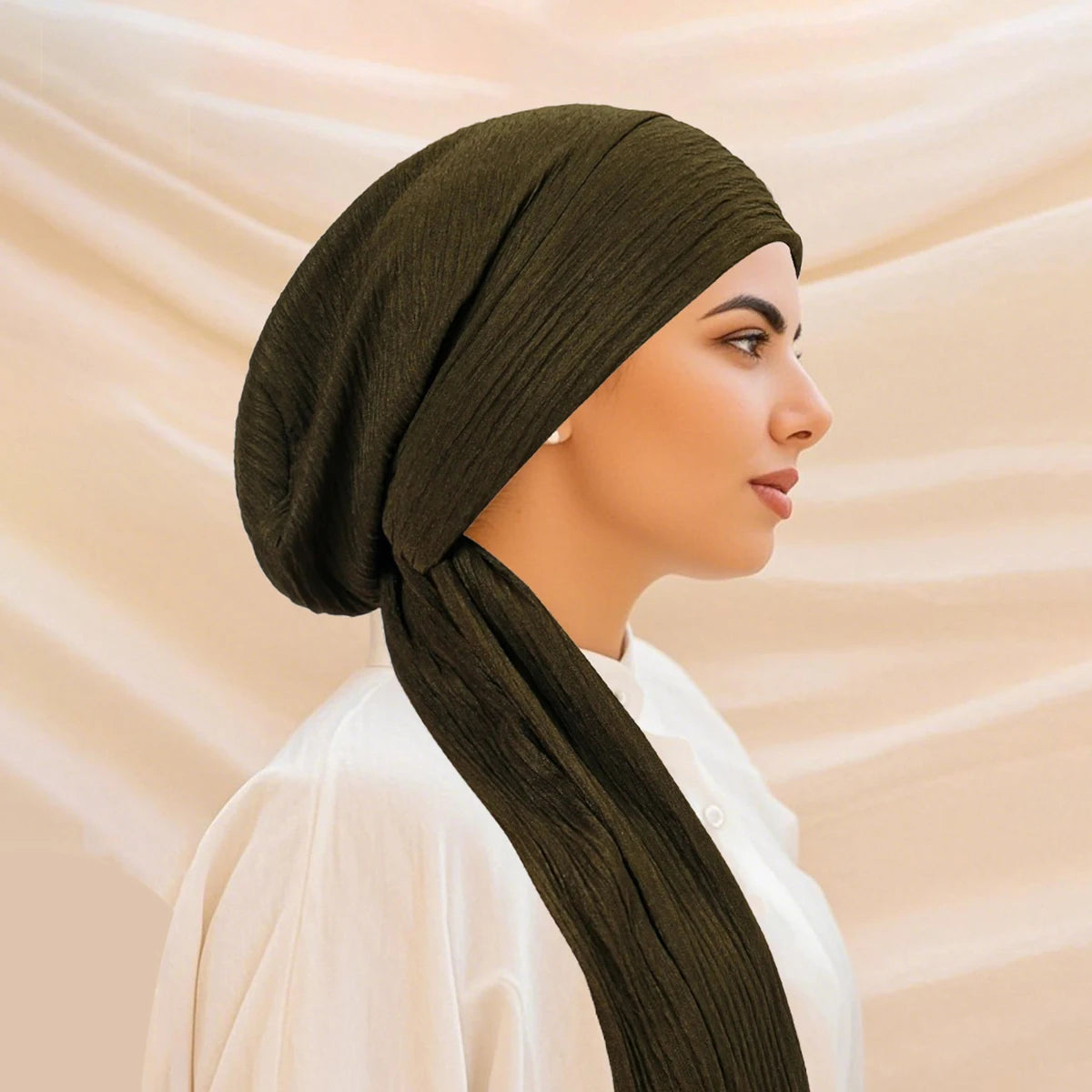 A woman wearing a solid olive green turban hijab cap and white top, shown in profile.