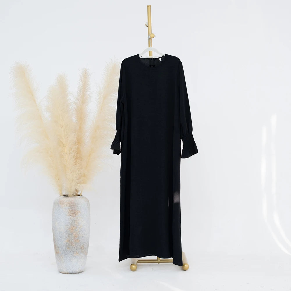 Vestido abaya negro holgado con puños fruncidos colgado en una percha