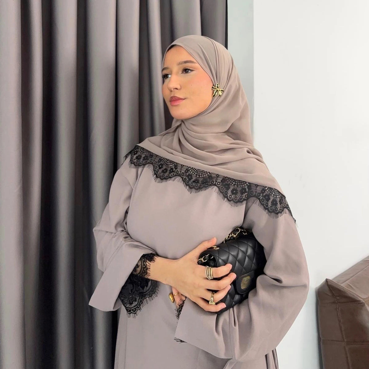 Una mujer vistiendo un conjunto de abaya de encaje beige con hijab, de pie en interiores.