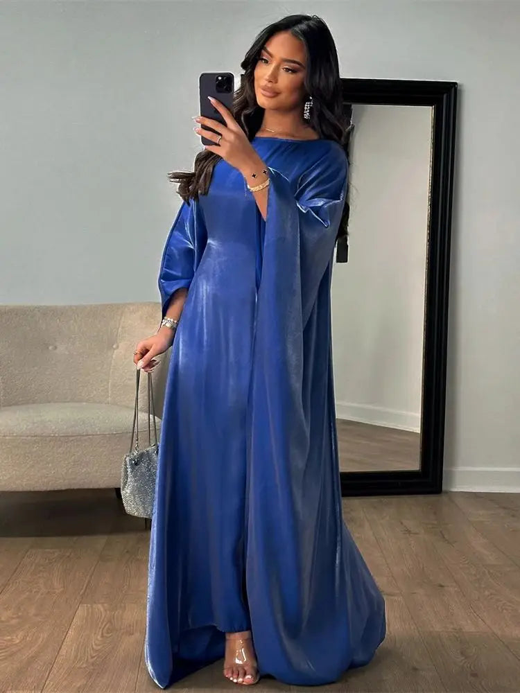 Una mujer modela un vestido abaya de satén azul real con vuelo en un estudio.