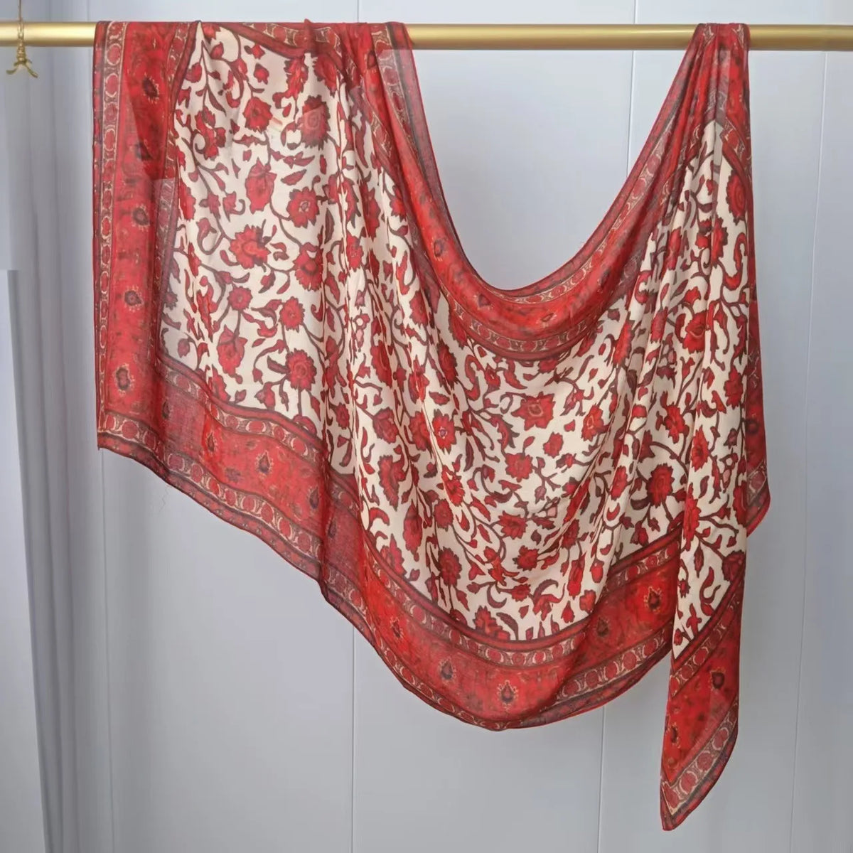 Fließender roter und cremefarbener gemusterter Hijab-Schal an einem Holzbügel.
