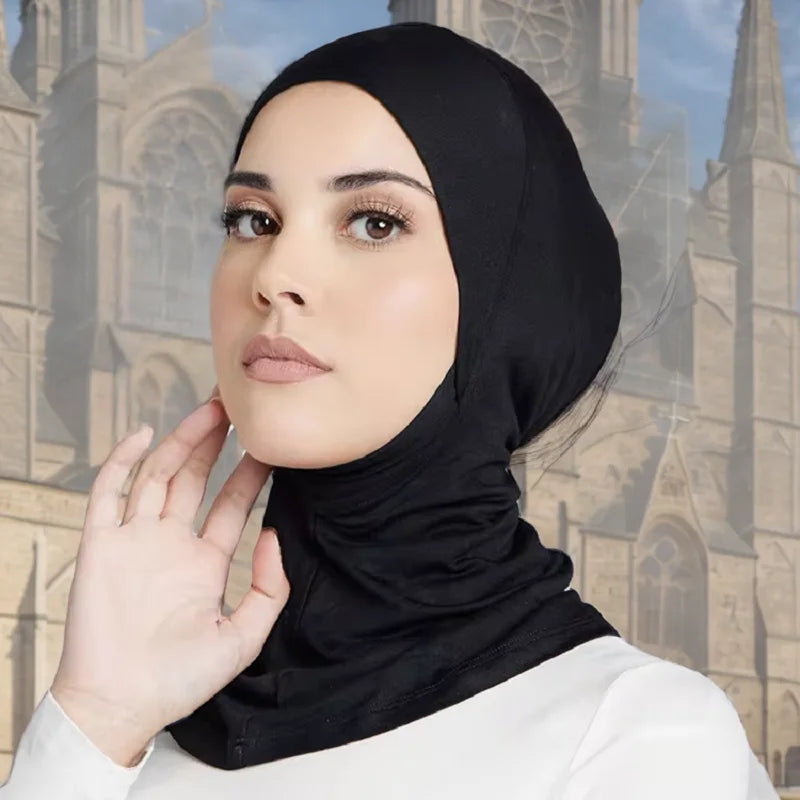 Eine Frau trägt eine schwarze, dehnbare Baumwoll-Hijab-Kappe und blickt direkt in die Kamera.