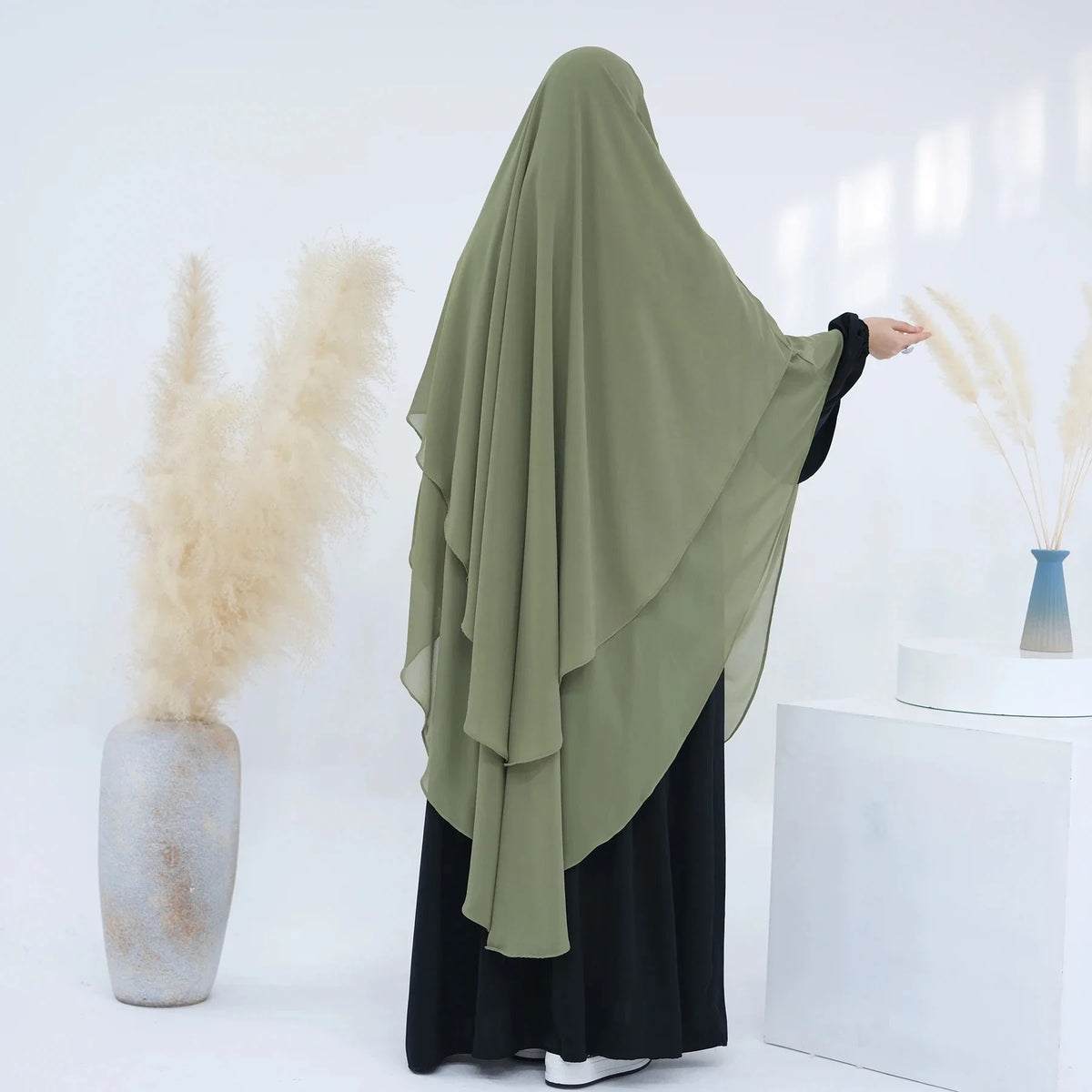 Eine Frau mit einem fließenden olivgrünen Chiffon-Niqab und schwarzer Kleidung vor weißem Hintergrund.