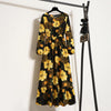 Schwarzes Maxi-Kleid mit leuchtend gelbem und braunem Blumenmuster an einem Kleiderständer.