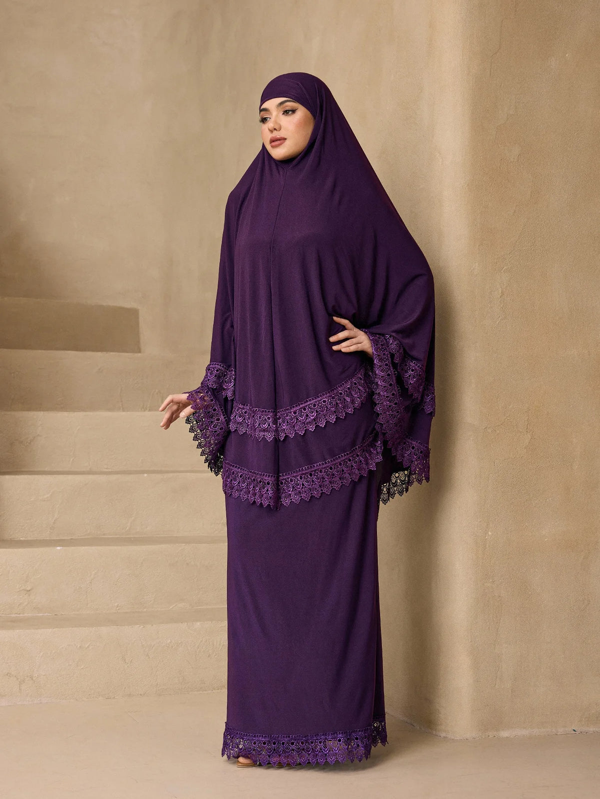 Eine Frau trägt ein elegantes, mehrlagiges Spitzen-Khimar-Abaya-Set in tiefem Violett vor neutralem Hintergrund.
