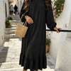 Une femme portant une longue robe bohème noire à volants marchant dans une ruelle de pierre.