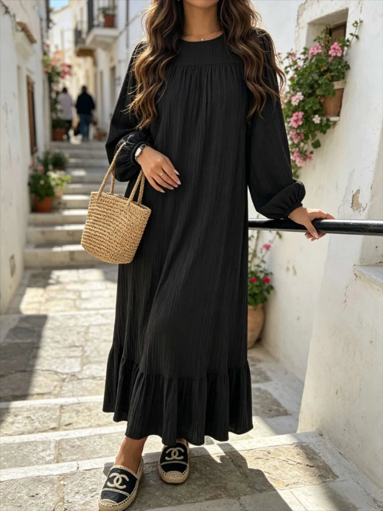 Une femme portant une longue robe bohème noire à volants marchant dans une ruelle de pierre.