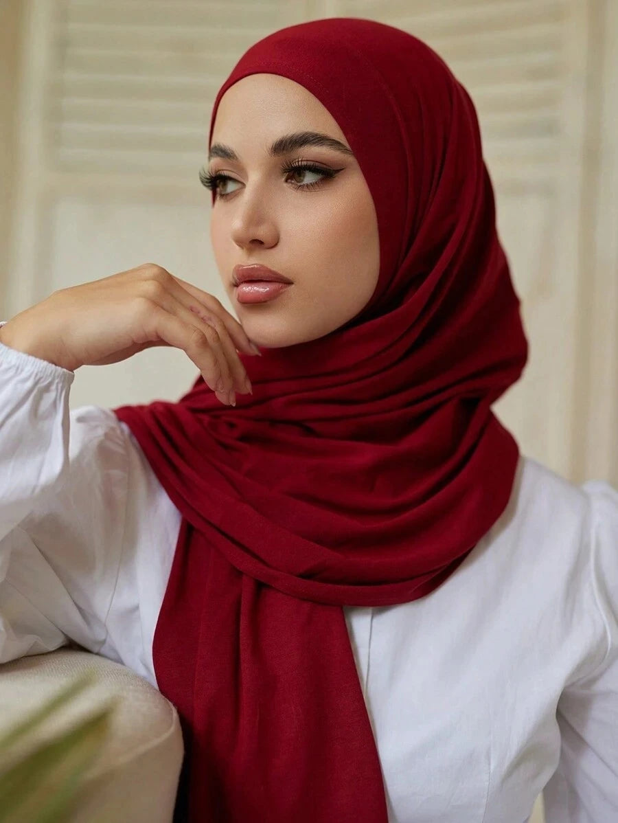 Una mujer vistiendo un pañuelo de jersey modal rojo intenso con una blusa blanca, mirando a un lado.