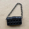 Bolso de cuero grabado de cocodrilo negro con correa de cadena plateada sobre fondo neutro.