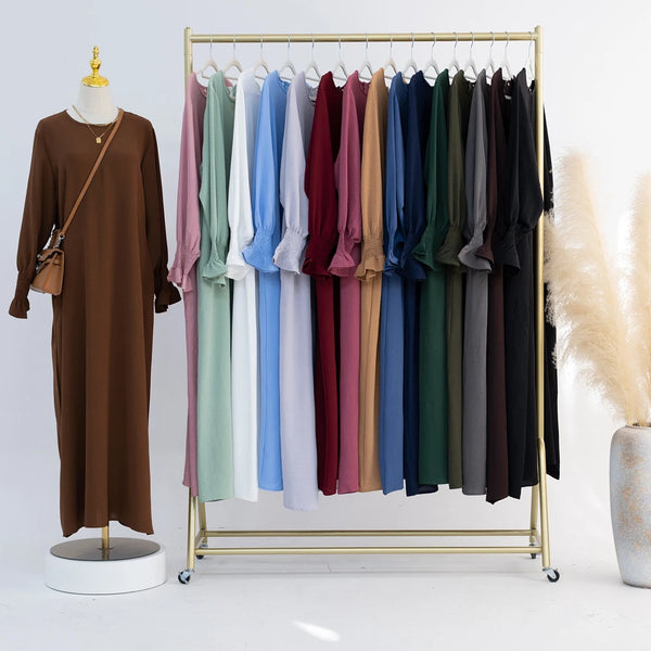 A rack displaying various loose-fit abaya dresses in shades of brown, pink, blue, and green.