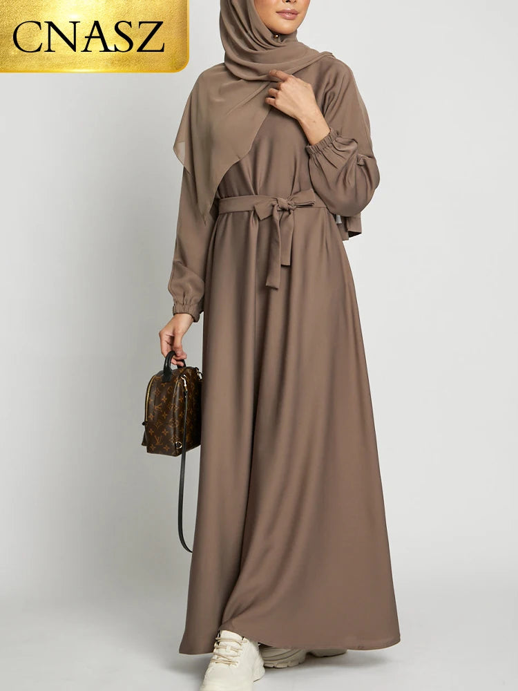 Eine Frau trägt eine lange, fließende taupefarbene marokkanische Kaftan-Abaya mit langen Ärmeln und geschnürter Taille.
