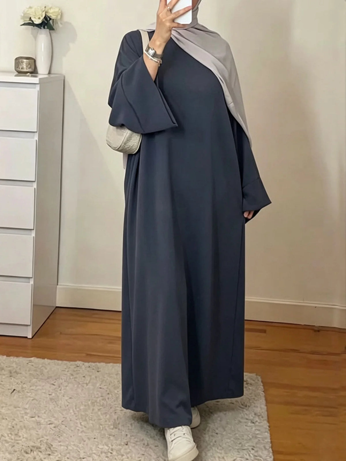 Une femme portant une longue abaya ample de couleur unie bleu-gris foncé avec des accents argentés.
