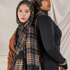 A woman wearing a plaid hijab scarf over a black top and brown garment.